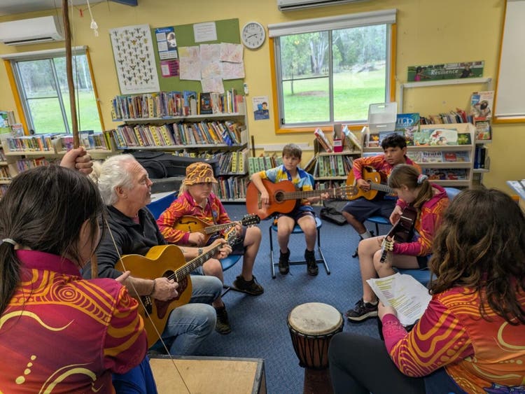 An image of a community member teaching students music for the end of year performance.
